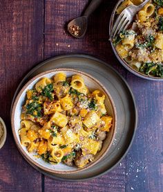 two bowls filled with pasta and spinach on top of a wooden table next to silverware