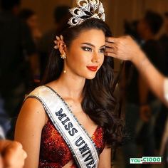 a beautiful young lady wearing a tiara and holding her hair in one hand while standing next to another woman