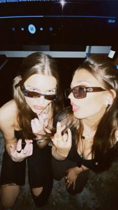 two young women posing for the camera in front of a television screen with their fingers up