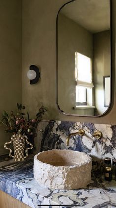 a bathroom sink with marble counter top and mirror above it, in front of a window