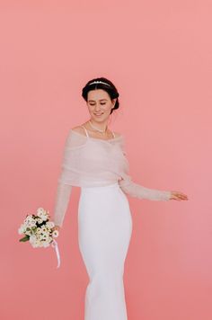 a woman in a white dress holding a bouquet and posing for the camera on a pink background