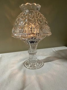 a clear glass candle holder sitting on top of a white tablecloth covered table cloth