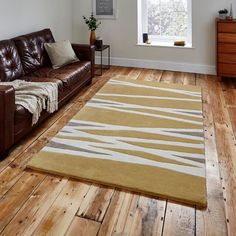 a brown leather couch sitting on top of a hard wood floor next to a window