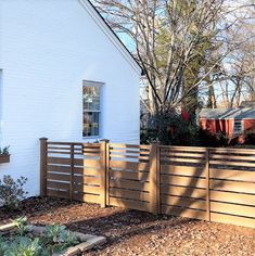 a white house with a wooden fence in front of it and some plants on the side