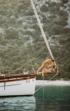 a man and woman are sitting on a sailboat in the water with trees behind them