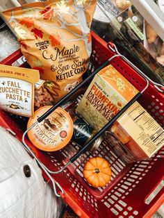 an orange shopping basket filled with food and some other items on top of a table