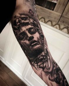 a man's arm with a black and grey tattoo on it, depicting the face of jesus