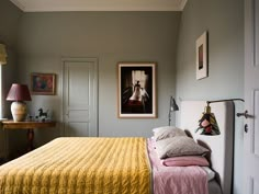 a bed sitting in a bedroom next to a painting on the wall and a lamp