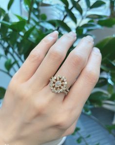 a woman's hand with a ring on it and a plant in the background