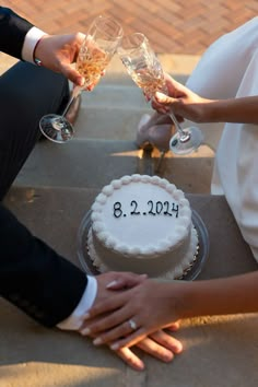 two people holding champagne glasses over a cake