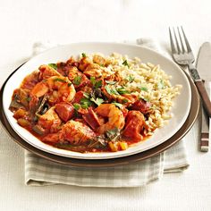 a white plate topped with shrimp and rice next to a fork, knife and spoon