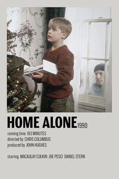 a young boy standing in front of a christmas tree holding a book and looking out the window