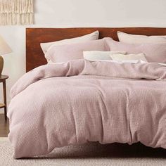 a bed with pink comforter and pillows in a white room next to a lamp