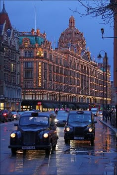 cars are driving down the street in front of an ornate building at dusk with lights on