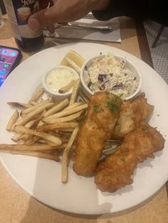 a white plate topped with fish and fries next to a bowl of coleslaw