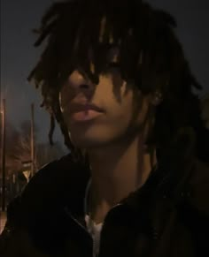 a young man with dreadlocks on his head looking off into the distance at night