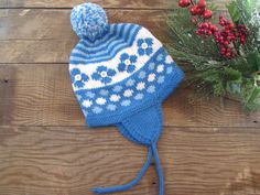 a blue and white knitted hat sitting on top of a wooden table next to flowers