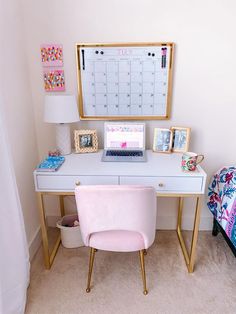 a white desk topped with a laptop computer next to a pink chair and wall mounted calendar