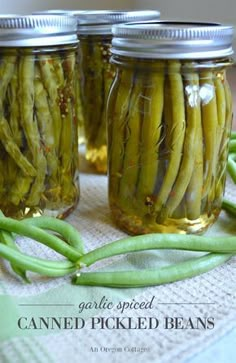 three jars filled with canned pickled beans on top of a cloth covered tablecloth