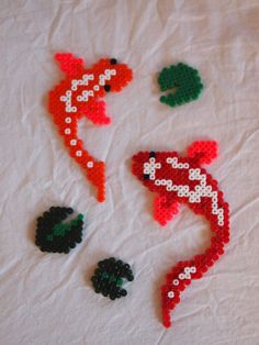 two red and one green fish made out of plastic beads on a white sheet with leaves