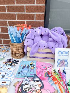 some purple stuffed animals are sitting on a table with other toys and books in front of a brick wall