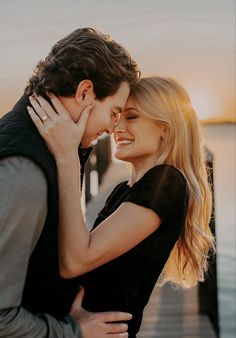 a man and woman embracing each other on a pier near the water at sunset or sunrise