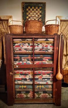 an old wooden cabinet with quilts and baskets on top