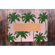 a pink and green welcome mat with palm trees in the background on a wooden wall