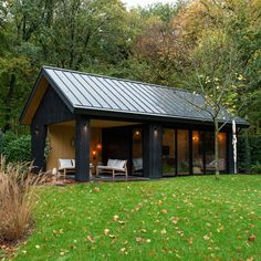 a small black cabin in the middle of a field with chairs and trees around it