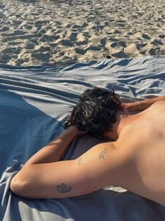 a man laying on top of a beach next to the ocean with his back turned