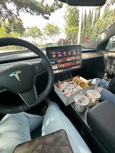 a person sitting in the driver's seat of a car with food and drinks