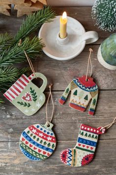 christmas stockings and mittens ornament hanging on a wooden table next to a candle