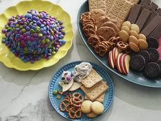 two plates filled with cookies, crackers and pretzels next to each other