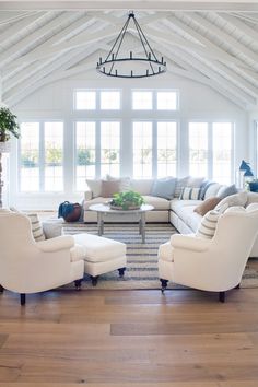 a living room filled with furniture and a chandelier hanging from the ceiling in front of large windows