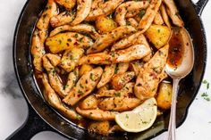 chicken and potatoes in a skillet with lemon wedges