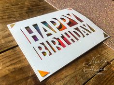 a card with the words happy birthday cut out on it sitting on top of a wooden table