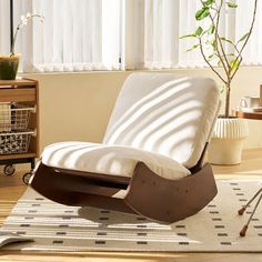 a rocking chair in front of a window with blinds on the windowsill, next to a potted plant