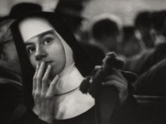 black and white photograph of a nun holding her hand up to her face with other people in the background