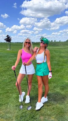 two women standing next to each other on top of a grass covered golf course, one in pink and the other in green