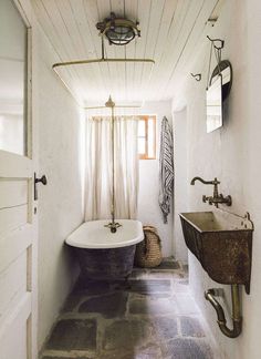 an old fashioned bathtub and sink in a bathroom with white walls, stone flooring and exposed wood ceiling