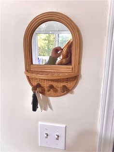 a wooden mirror hanging on the wall next to a light switch with a person's reflection in it