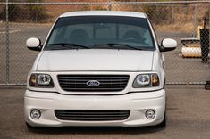 the front end of a white van parked in a parking lot next to a chain link fence