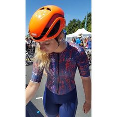 a woman wearing an orange helmet and blue cycling shorts is looking down at her bike