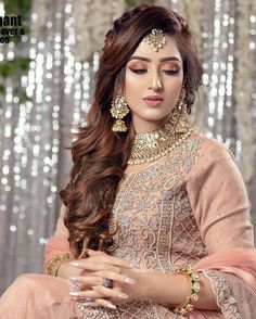 a woman in a pink outfit with long hair and gold jewelry on her head, sitting down