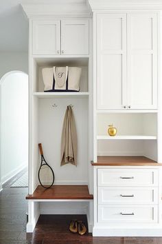 a tennis racket is sitting on the bench in this white closet with built - in shelves