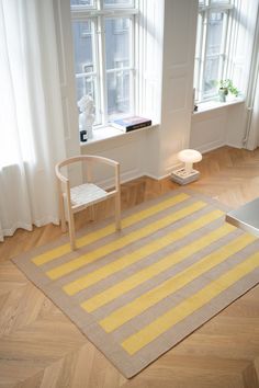 a yellow and grey rug in front of a window with a chair on the floor