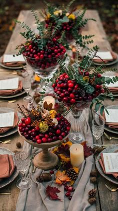 a table topped with lots of red berries and greenery next to glasses filled with candles