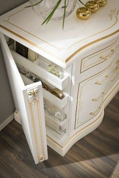 a white cabinet with gold trim and drawers in a room that has wood flooring