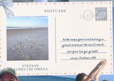 two girls holding up a postcard with the word love written on it and hearts in the sand