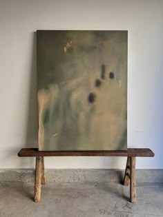 a painting sitting on top of a wooden bench in front of a white wall and concrete floor